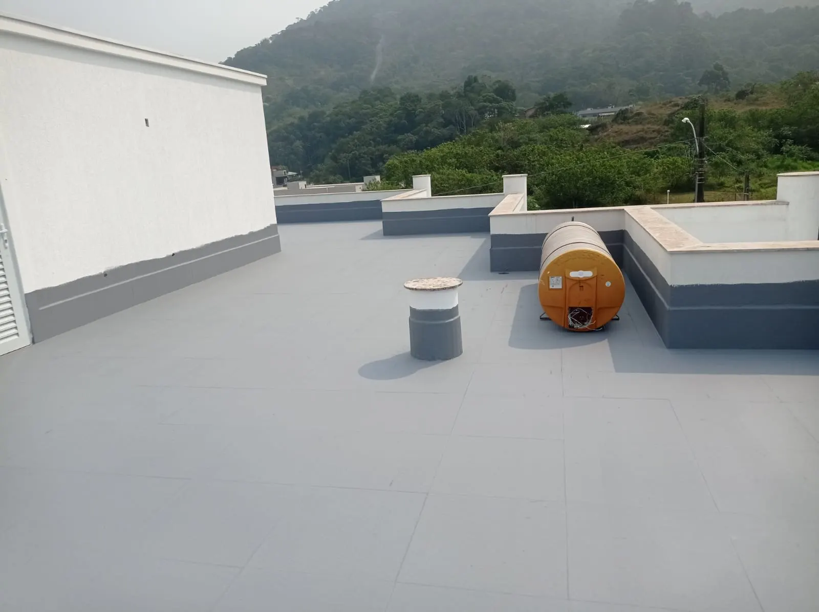 Laje/terraço impermeabilizado com acabamento cinza contínuo, caixa d’água e vista para morros