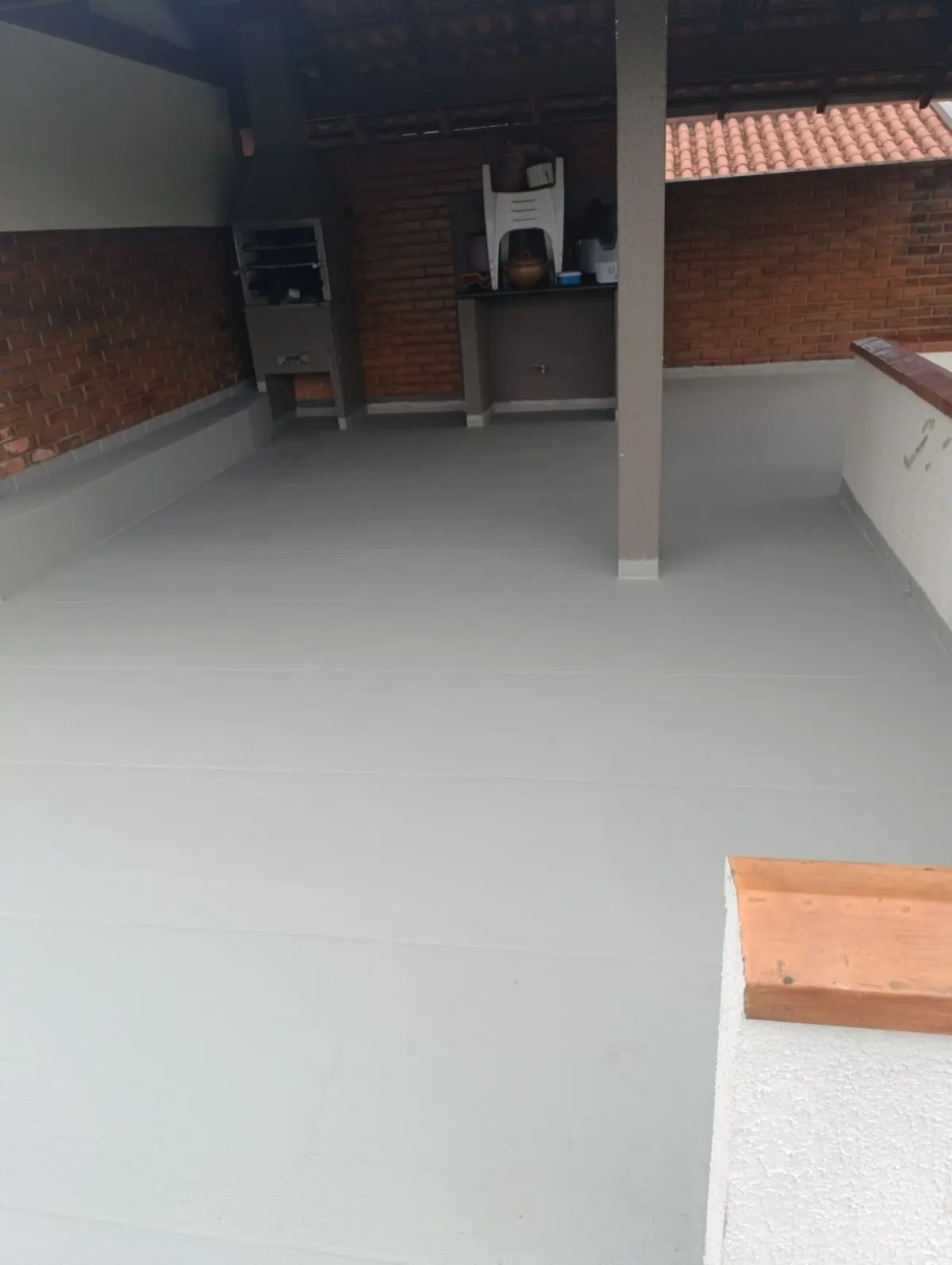Terraço coberto com churrasqueira e piso impermeabilizado cinza contínuo — sem demolição total
