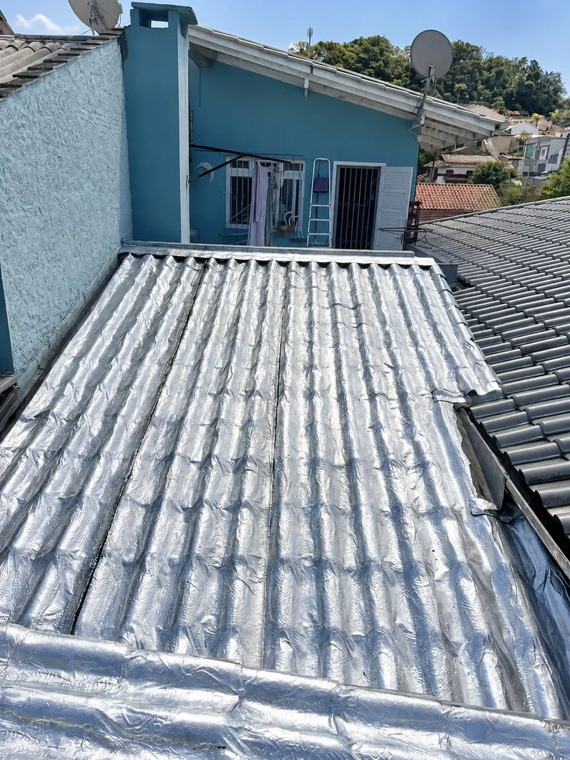 Membrana aluminizada em telhado residencial junto a fachada azul e telhas vizinhas