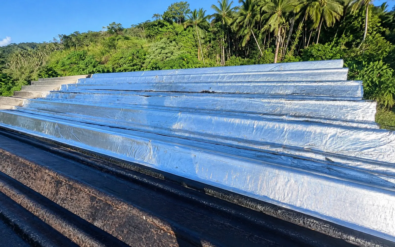 Membrana aluminizada em cobertura com vegetação e palmeiras ao fundo