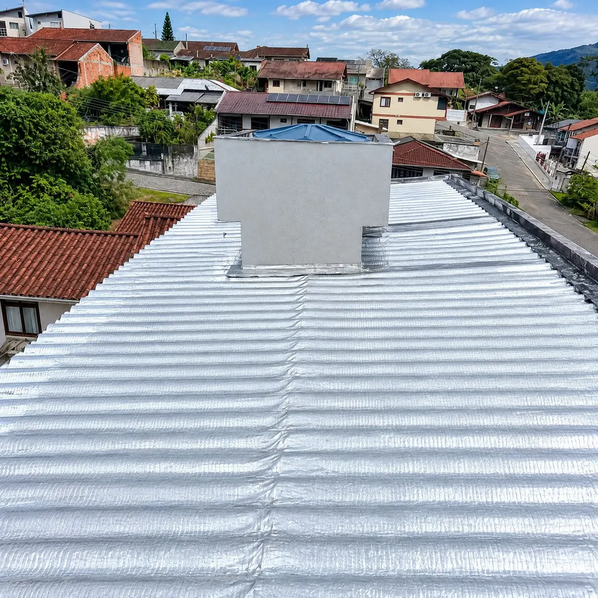 Vista frontal do telhado selado com manta asfáltica aluminizada e chaminé