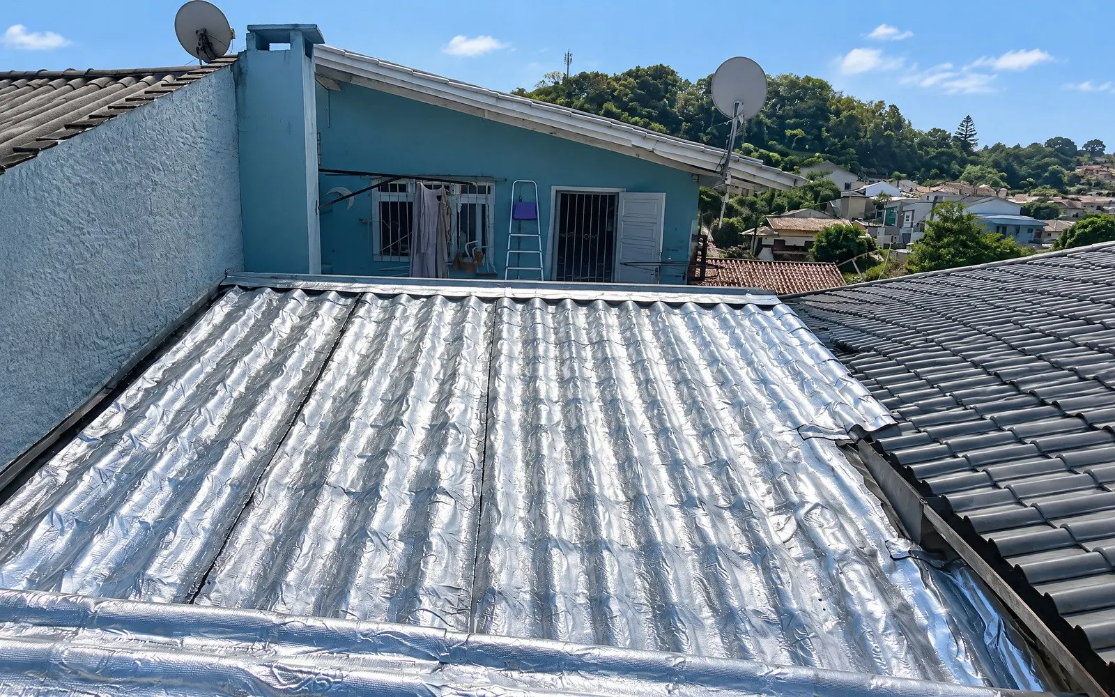 Telhado com manta aluminizada sob sol forte — arremates e encontro com alvenaria